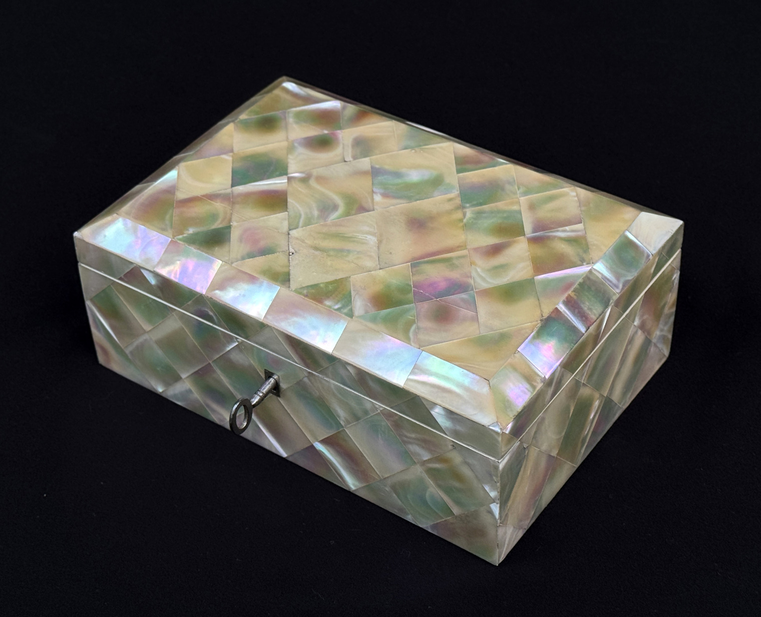 Front right view of an antique mother of pearl inlaid jewellery box with key inserted.