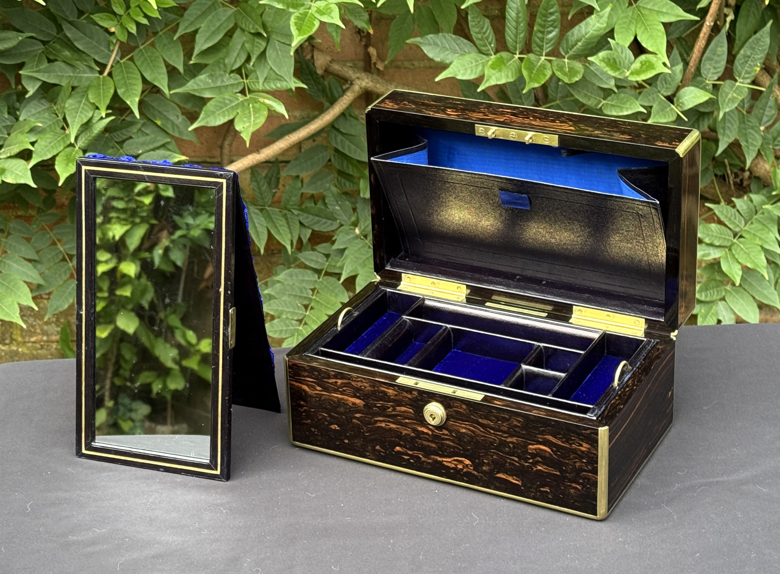 Front right internal view of an antique gentleman's travelling jewellery box in coromandel, by Houghton & Gunn, with free-standing mirror on display outside of the box.
