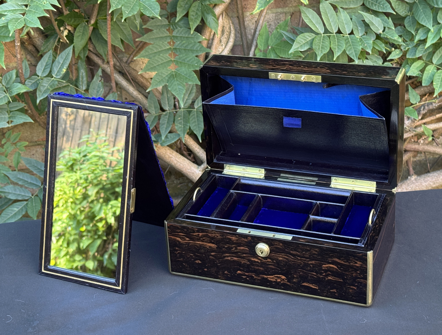 Front right internal view of an antique gentleman's travelling jewellery box in coromandel, by Houghton & Gunn, with free-standing mirror on display outside of the box.