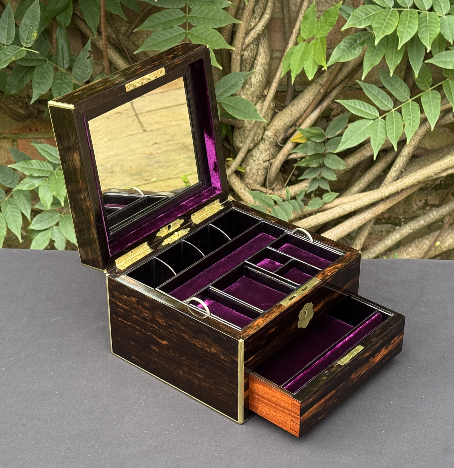 Left side interior view of a miniature antique jewellery box in coromandel, by George Betjemann & Sons, with lower drawer extended and mirror panel on display.