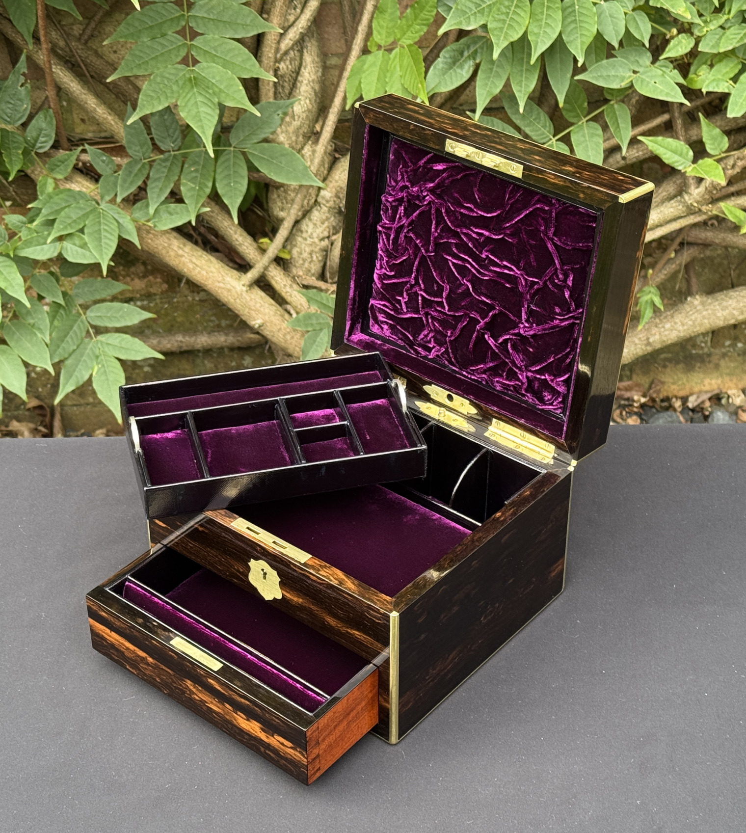Front right interior view of a miniature antique jewellery box in coromandel, by George Betjemann & Sons, with lower drawer extended and jewellery tray partially removed.